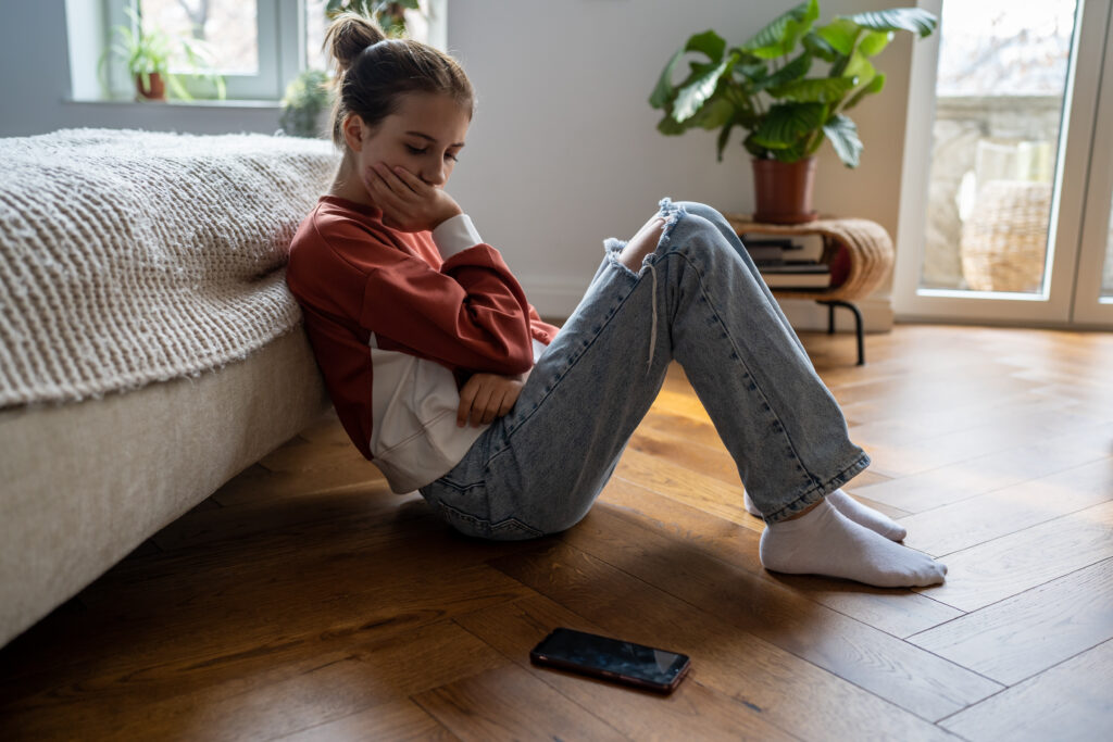 Teenage girl in her room with a phone beside her, representing online exploitation