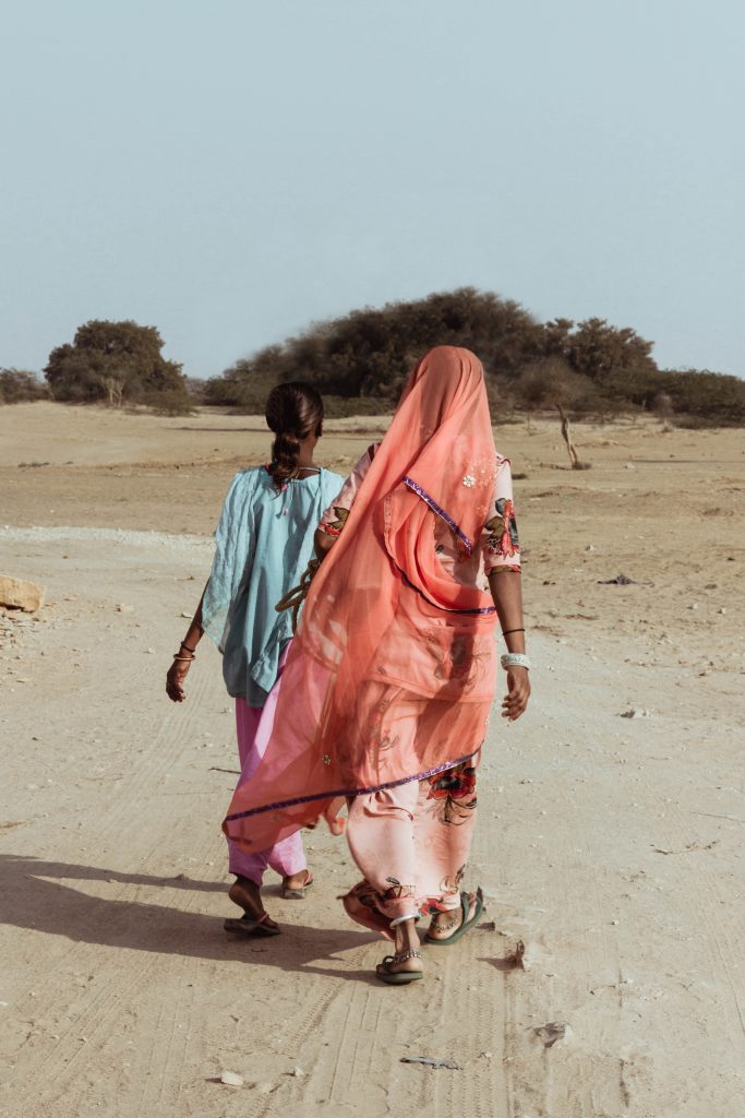 One woman walks in a saree with back to camera. Second woman walks beside, but in front, of her.