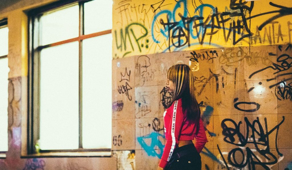 young Latin American woman standing alone near a wall of graffiti, representing the connection between human trafficking and immigrants