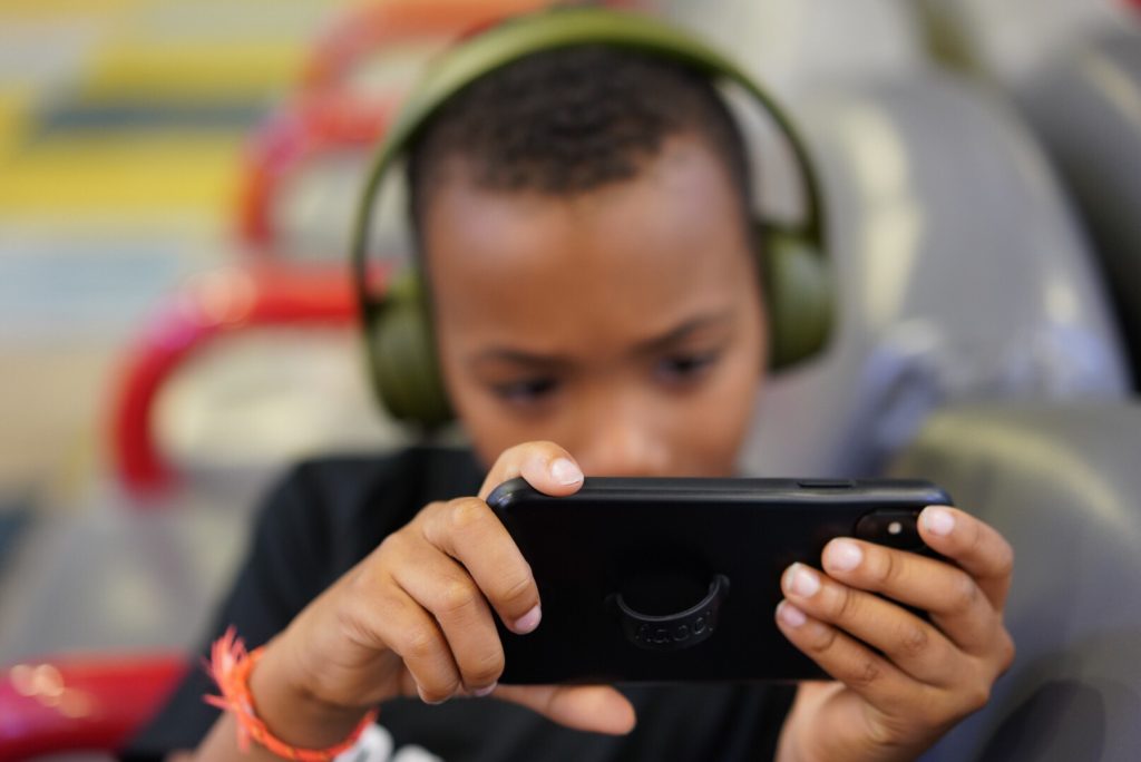boy wearing headphones and using a smartphone, illustrating the importance of teaching young people internet safety tools