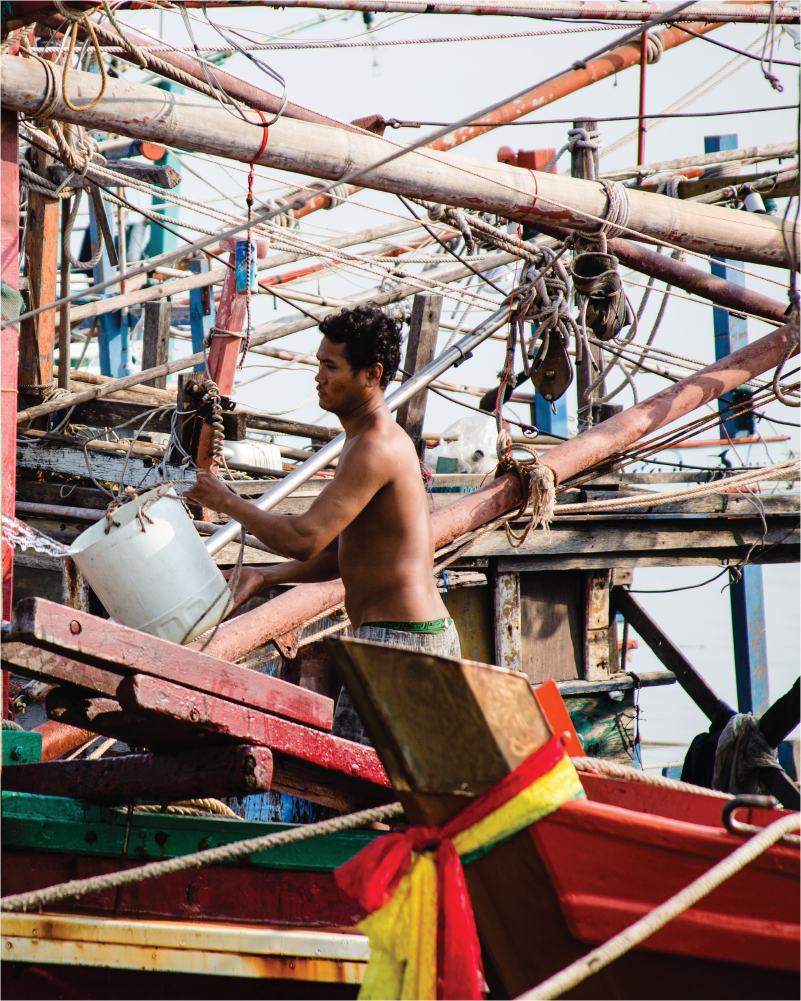 Shirtless SE Asian man carries a bucket while working on a boat.