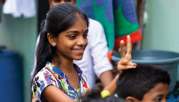 A moça na Índia sorri e faz um sinal de paz com os dedos.