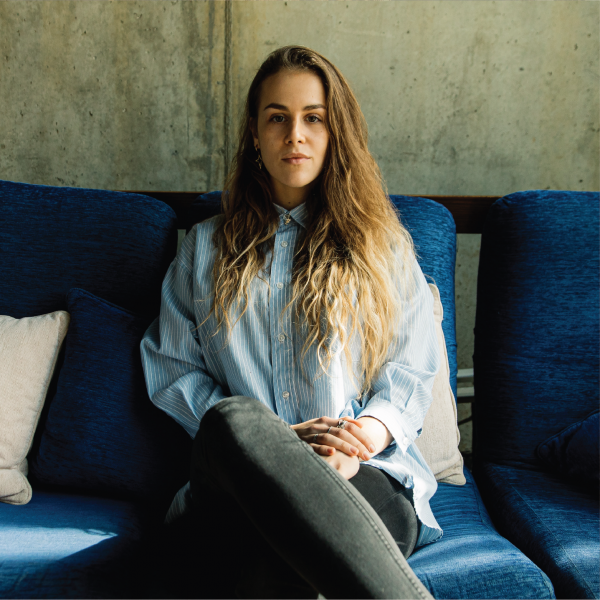 Jovem profissional feminina senta-se em um sofá azul, sorrindo para a câmera.