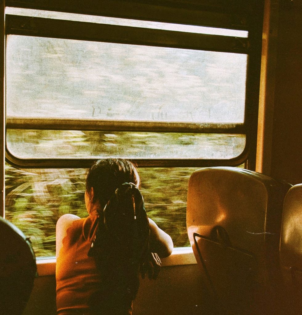 Young female Thai survivor sits looking out the window of a train.
