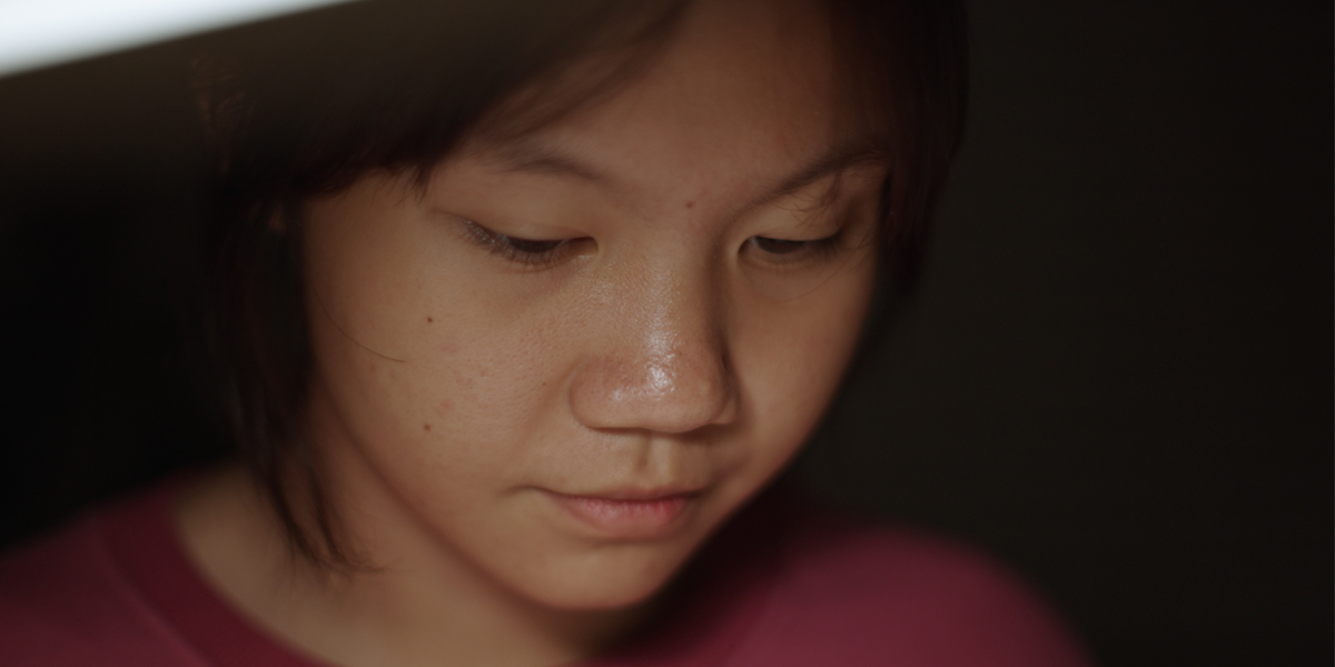 Young woman looks down away from camera, representative survivor of human trafficking