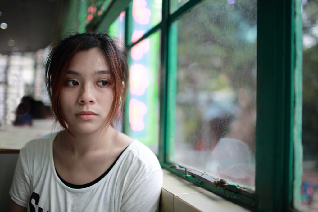 Young Asian woman looks out a window, representative image of a trafficking survivor