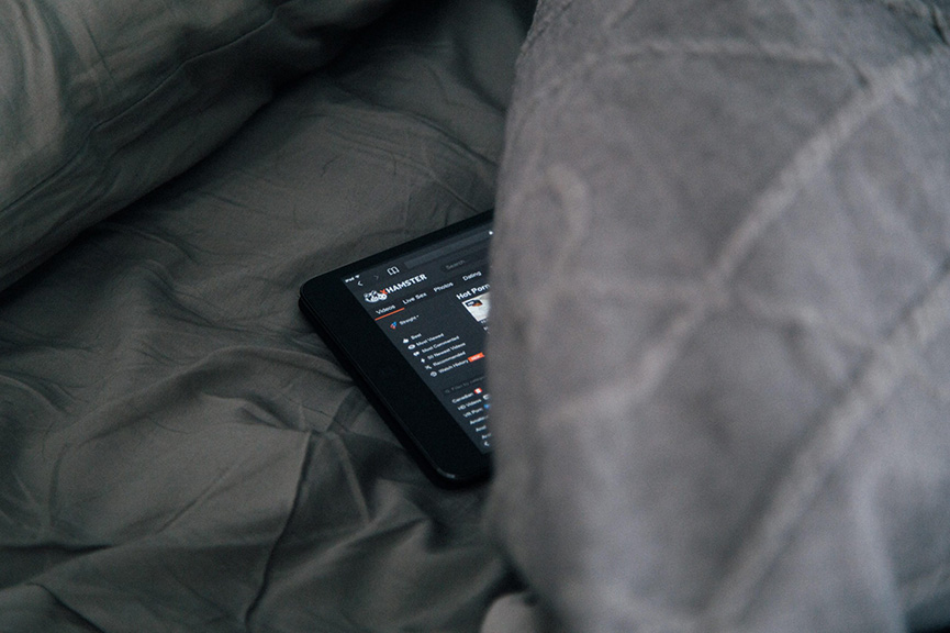 A phone emerges from underneath a blanket on a bed.