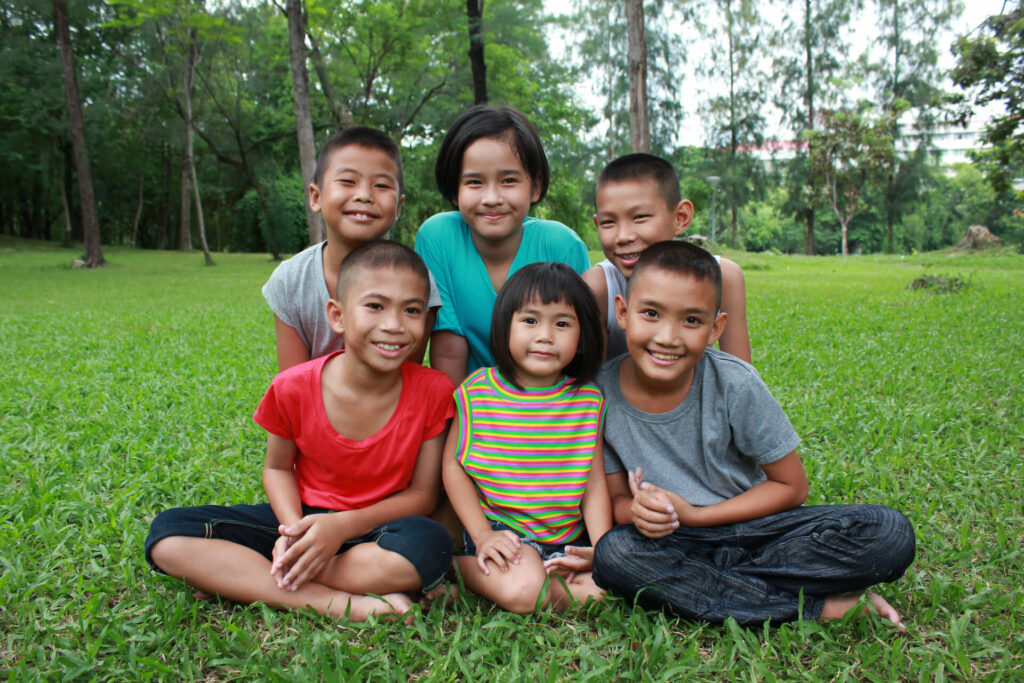 a group of Thai children sitting in the grass and smiling, showing the type of people we are looking to serve at The Exodus Road Thailand