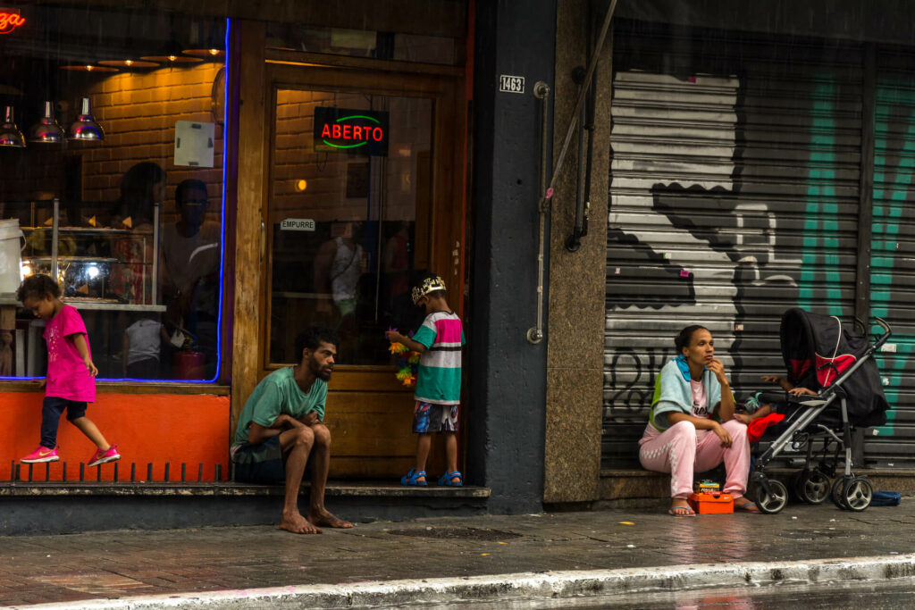 a young man and children sit on the side of a street in Sao Paulo, representing the reality of human trafficking in Brazil