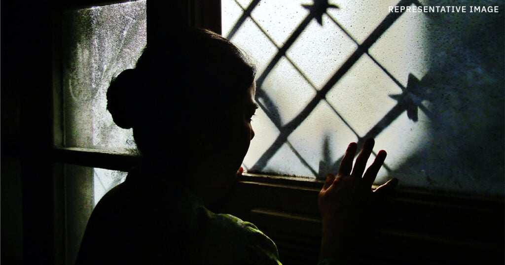 Indian girl looking out of a dark window, representing the confinement faced by the survivors from Operation 45 Minutes