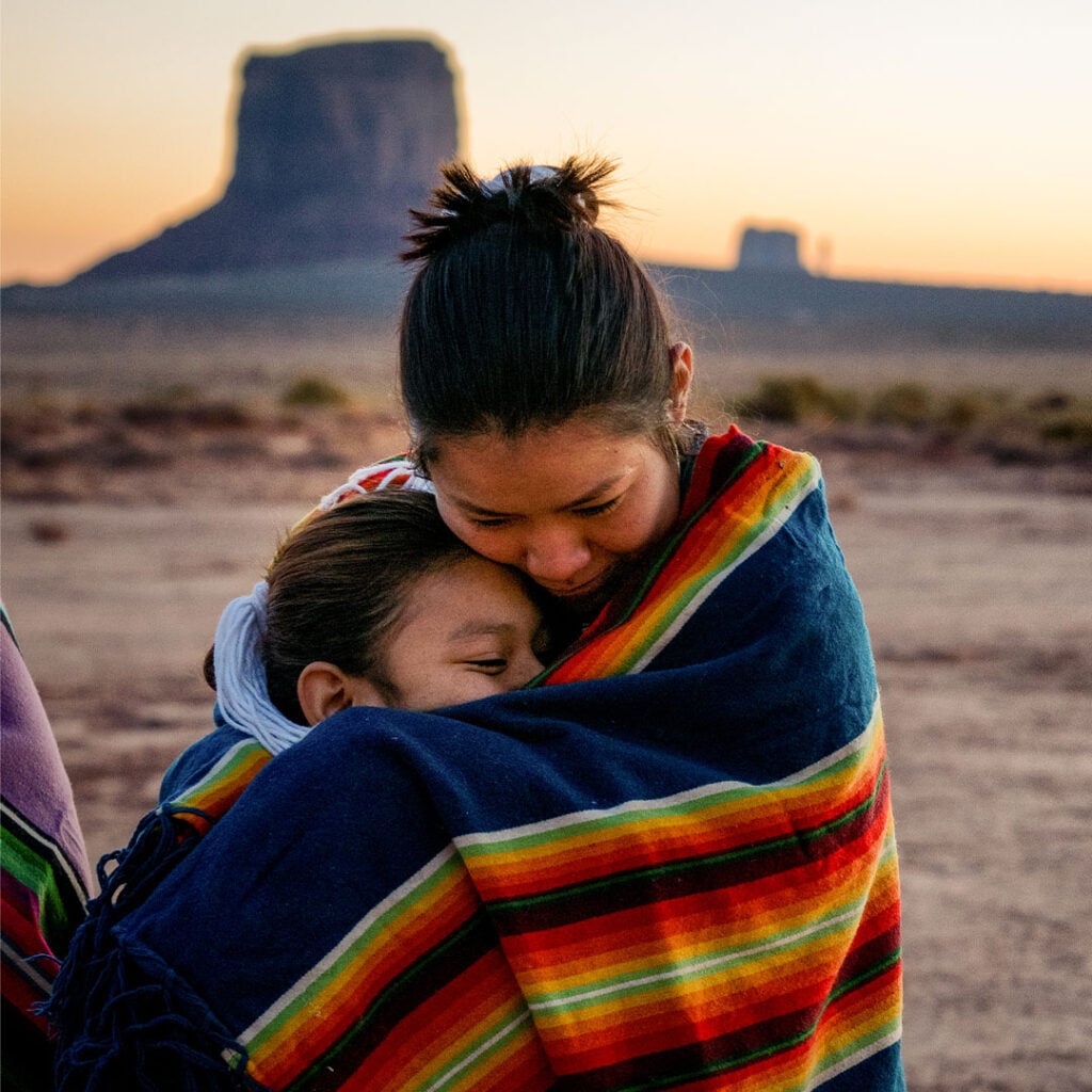 two young Native American girls standing and hugging in a desert landscape, representing the vulnerability of Native American communities to the horrors of human trafficking