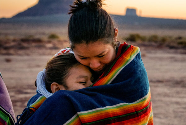 duas meninas nativas americanas em pé e abraçadas em uma paisagem desértica, representando a vulnerabilidade das comunidades nativas americanas aos horrores do tráfico humano