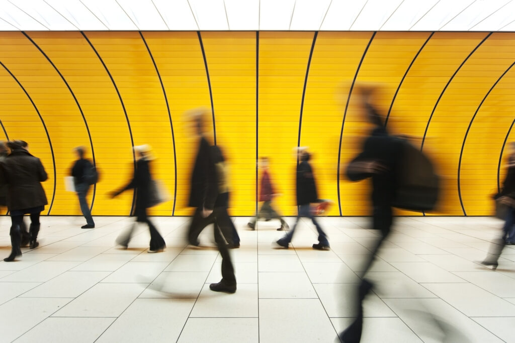 Motion blurred crowd of people walking by a yellow wall