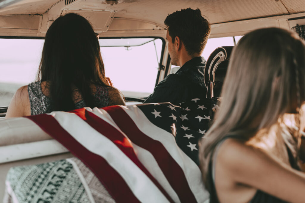 Human trafficking in the US represented by three young people sitting in a van, an American flag draped over the back of a seat