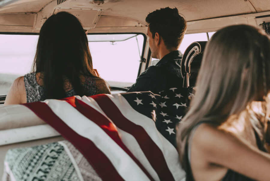 Human trafficking in the US represented by three young people sitting in a van, an American flag draped over the back of a seat