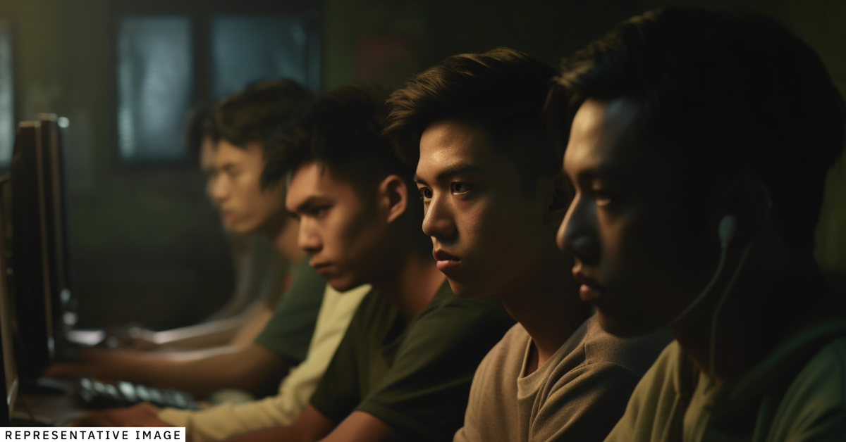 Several young men look at computer screens in a dark room.