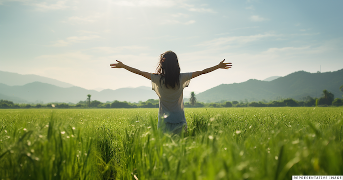 young Thai girl in a field with arms outstretched