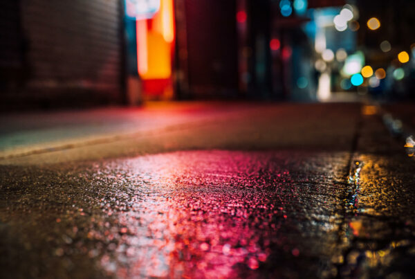 Red lights shine on wet pavement at night on a street.