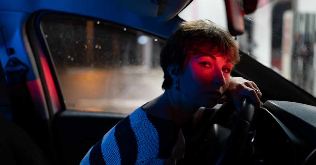 Young woman leans against a steering wheel at night