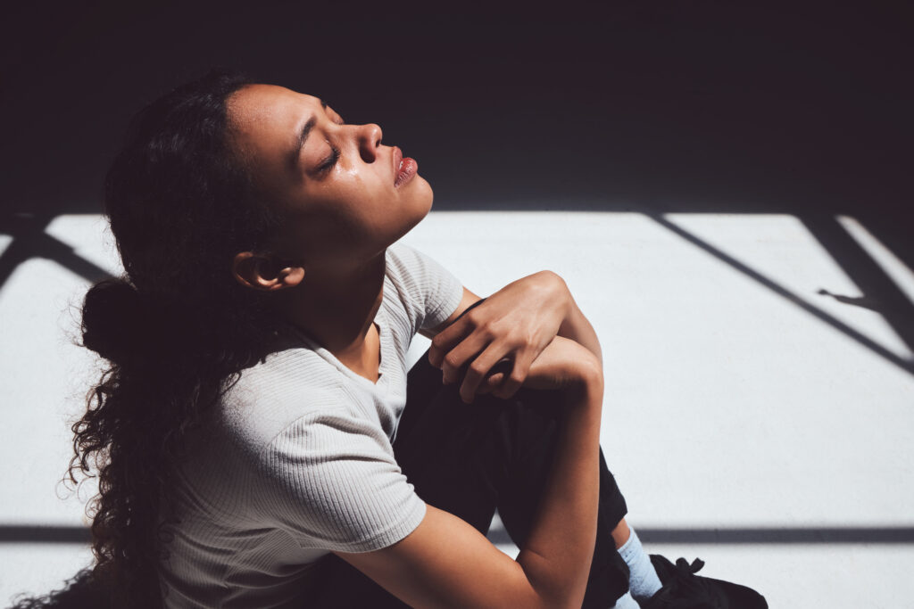 Depressed woman in an empty space looks up to the sun, eyes closed