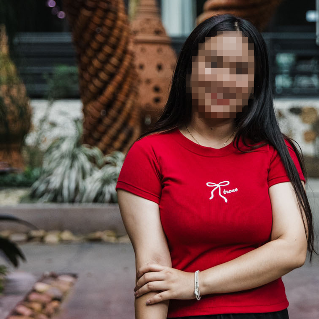 A young Thai woman who has survived human trafficking smiles at the camera, her face obscured for security