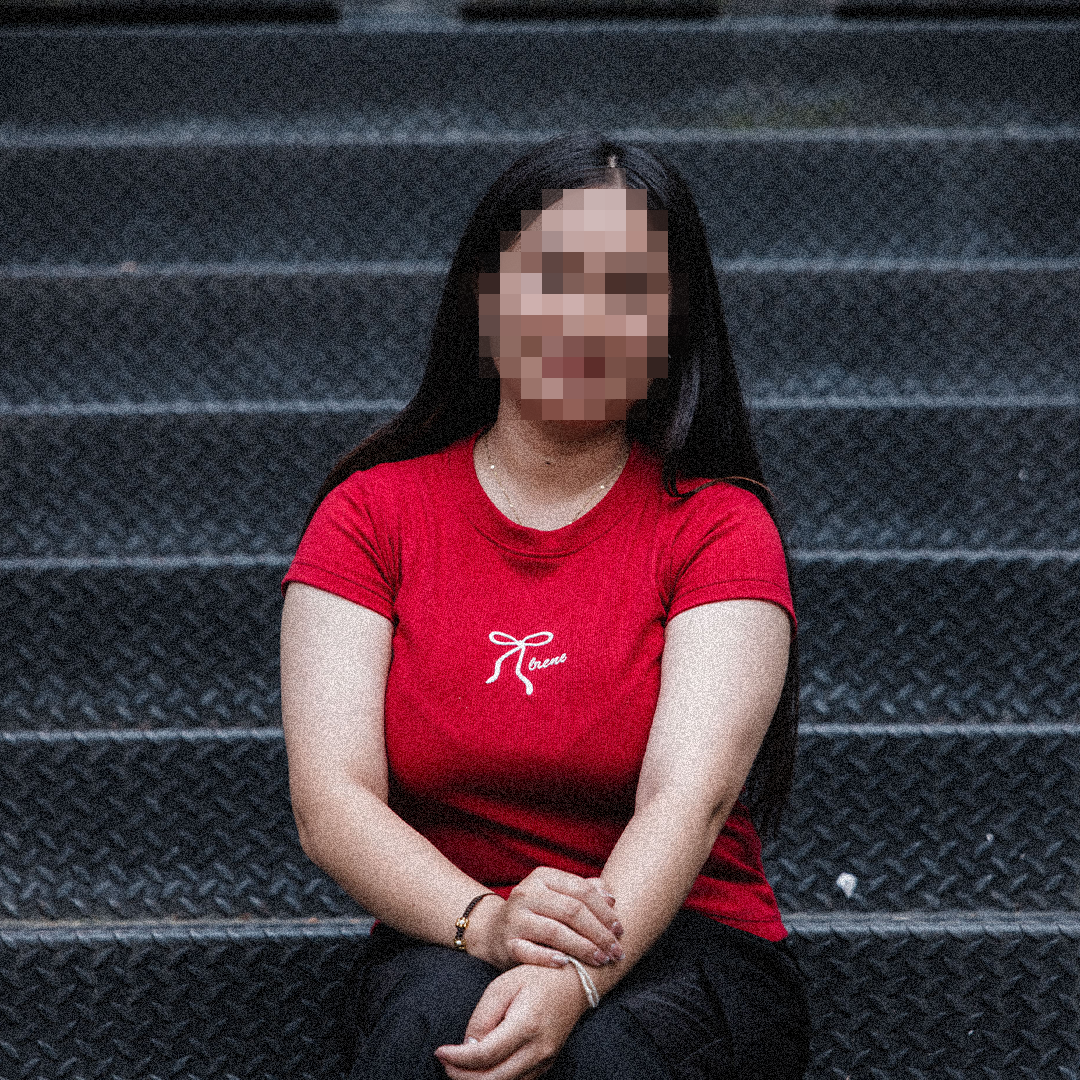 A survivor of sex trafficking sits on grey steps, her face blurred