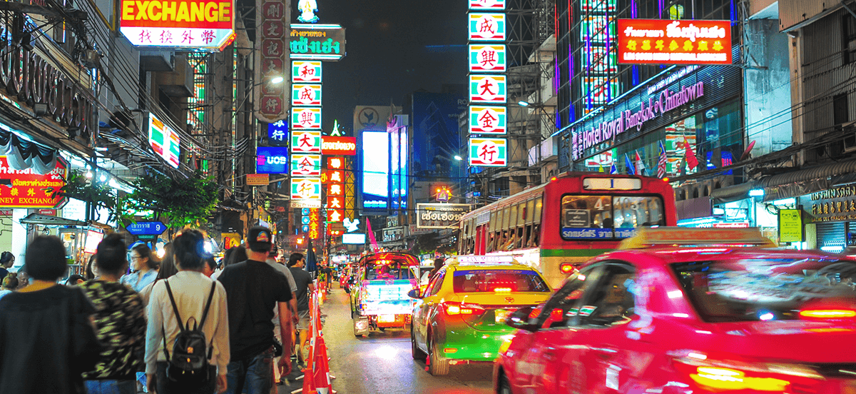 Busy Thailand street at night, colorful and lit up with signs and car lights.