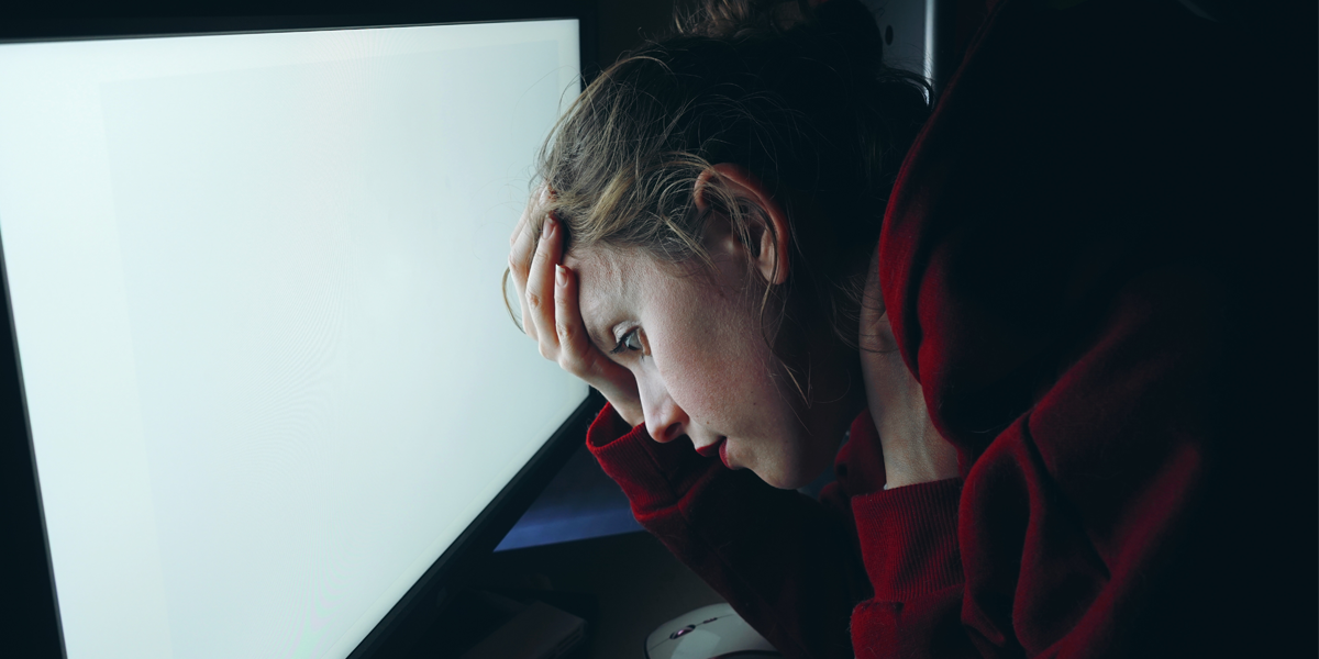 Young woman with head in hands in front of a computer screen