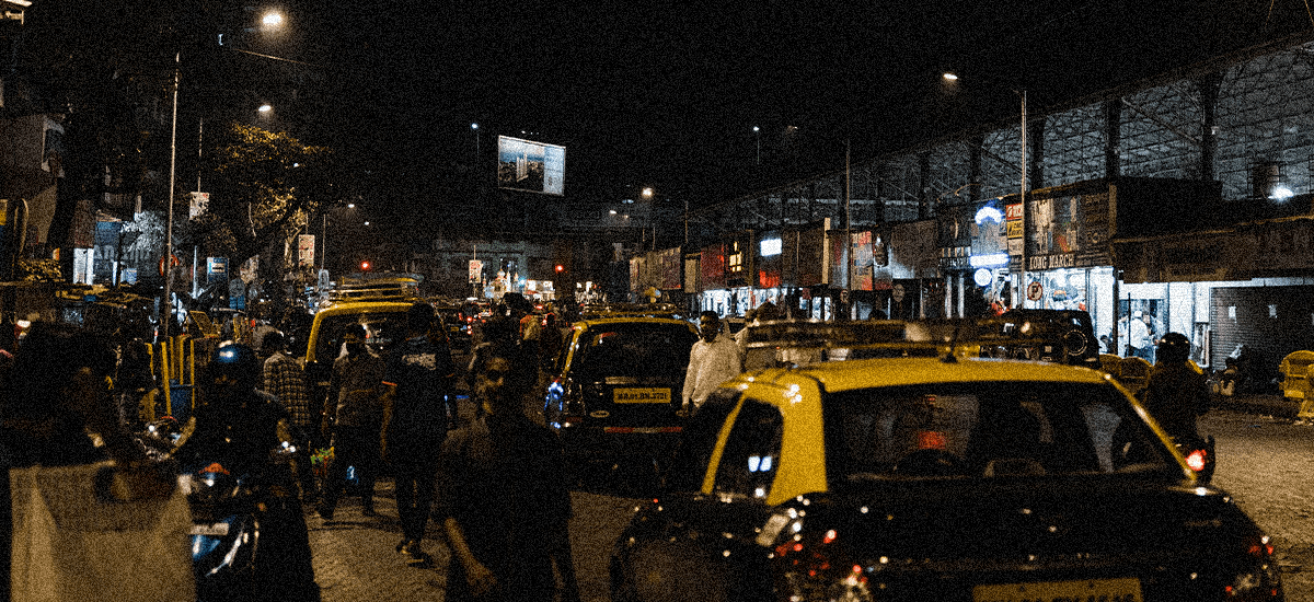 Busy street in India at night. People and taxi cabs compete for space in the crowded road.