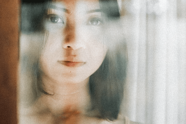 Thai young woman looks out from behind glass directly at camera.