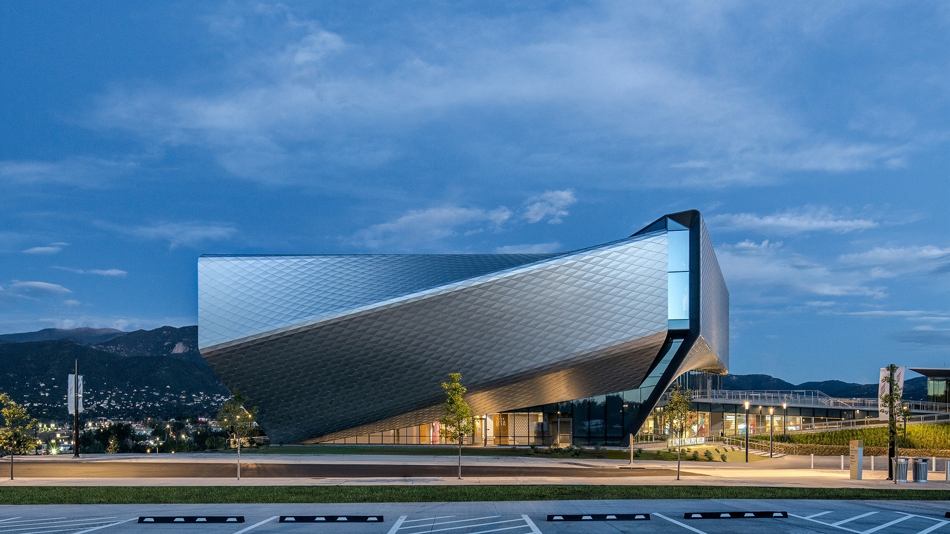 Exterior of the U.S. Olympic and Paralympic Museum at dusk, with mountains in the background.