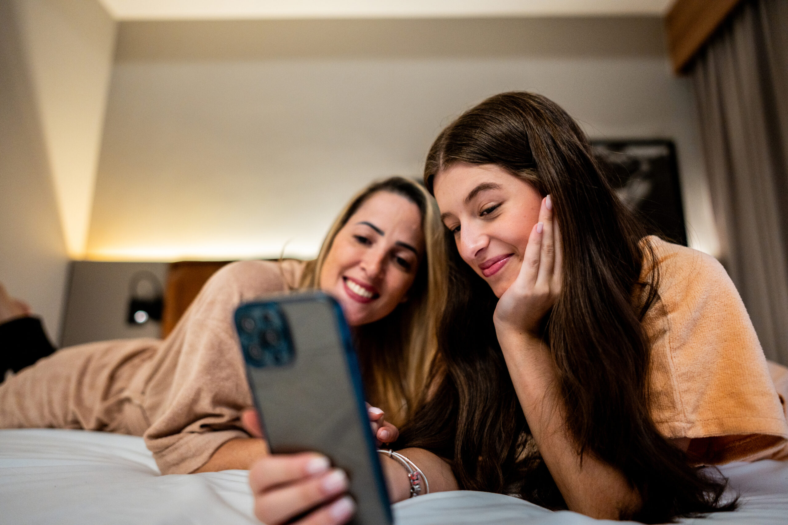 A mother and teenage daughter share a phone together, both smiling.