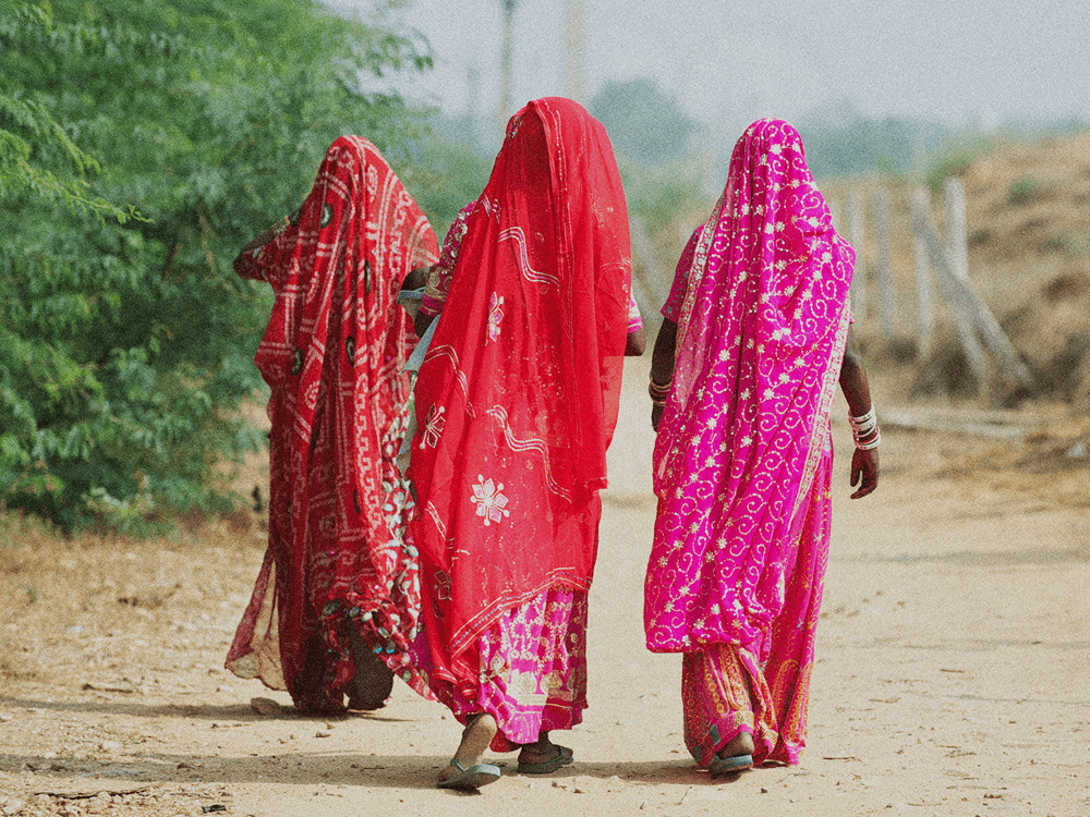 Indian women in colourful pink and red sari's walking away from camera