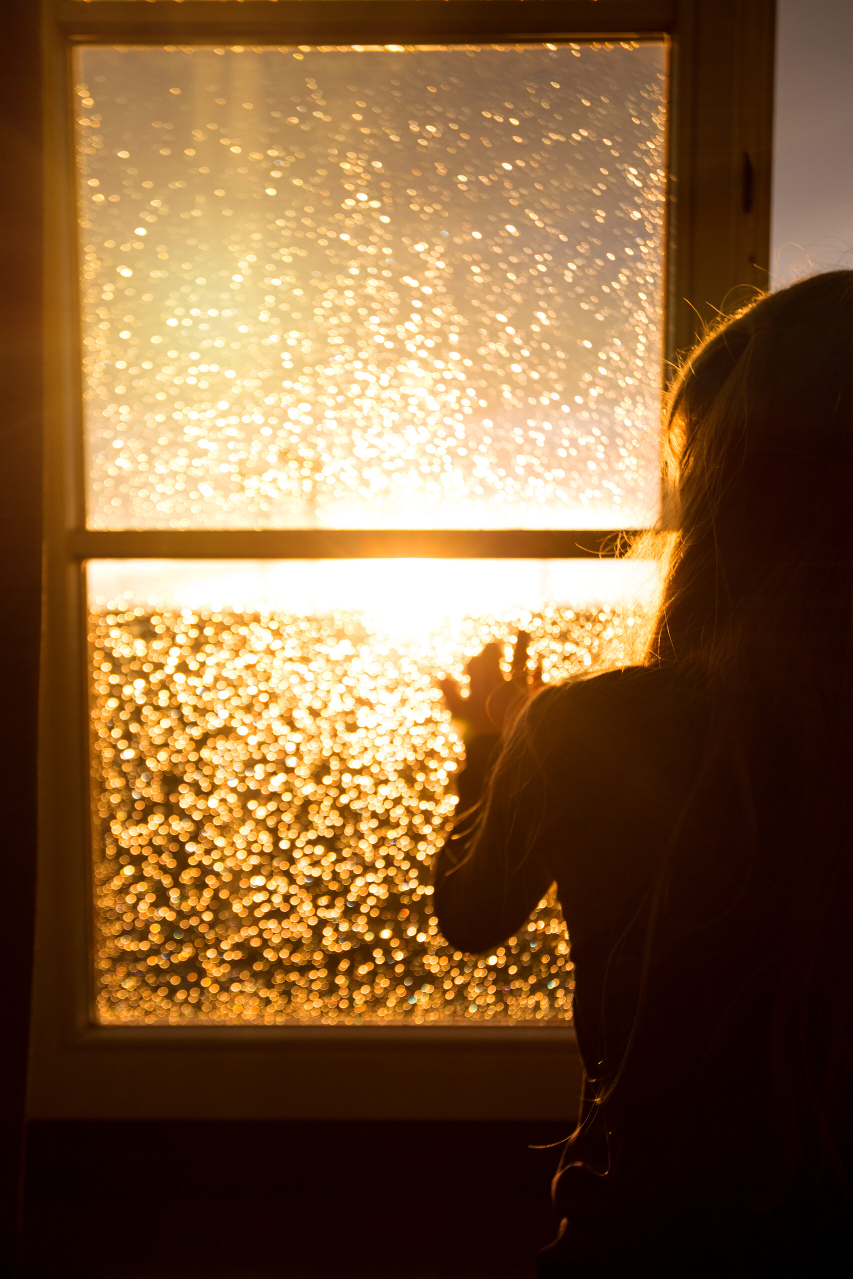 A woman looking out of a window at sunset.