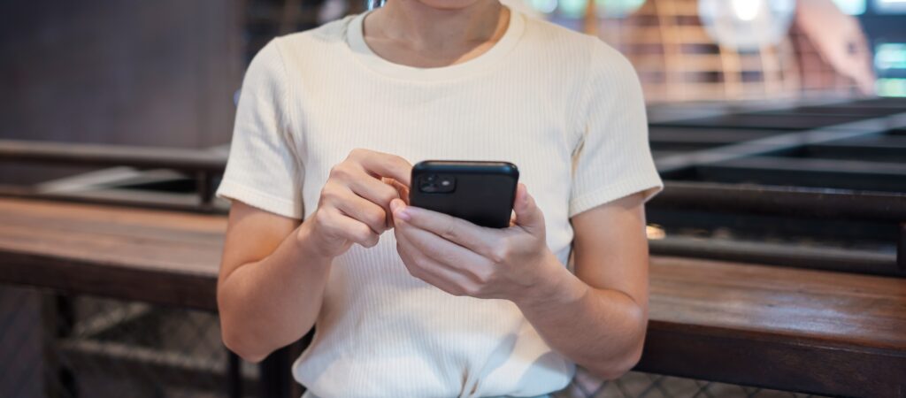 Young business woman using a black smartphone, representing someone scrolling through potentially false job offers