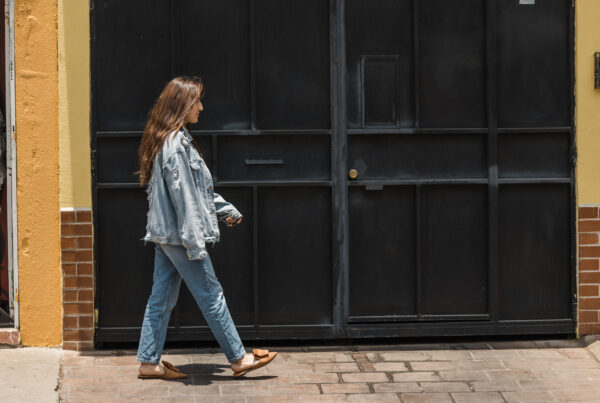 A young woman in Latin America wearing denim walks in front of empty glass doors