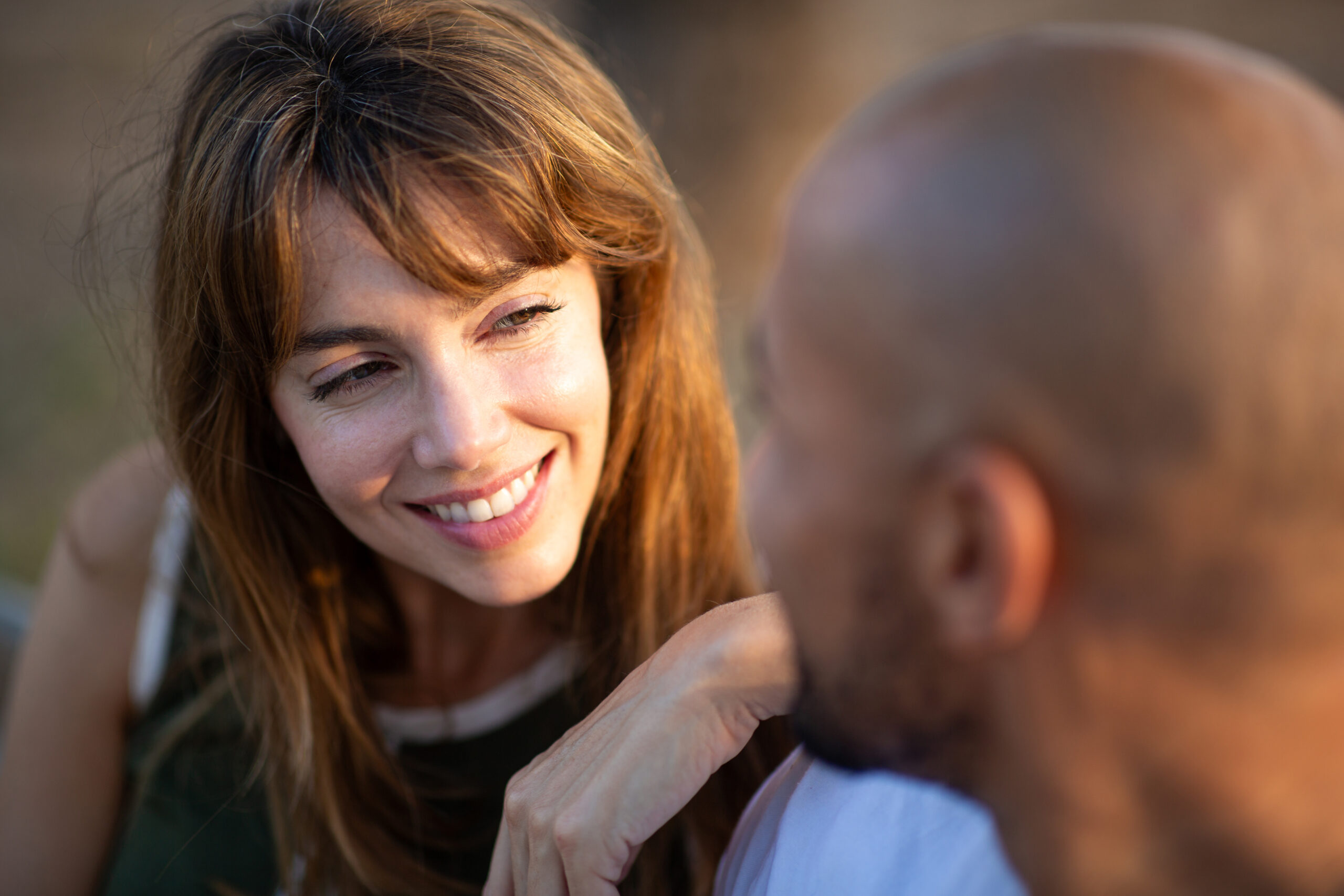 A woman smiling warmly at a man sitting close beside her, seen from behind his shoulder